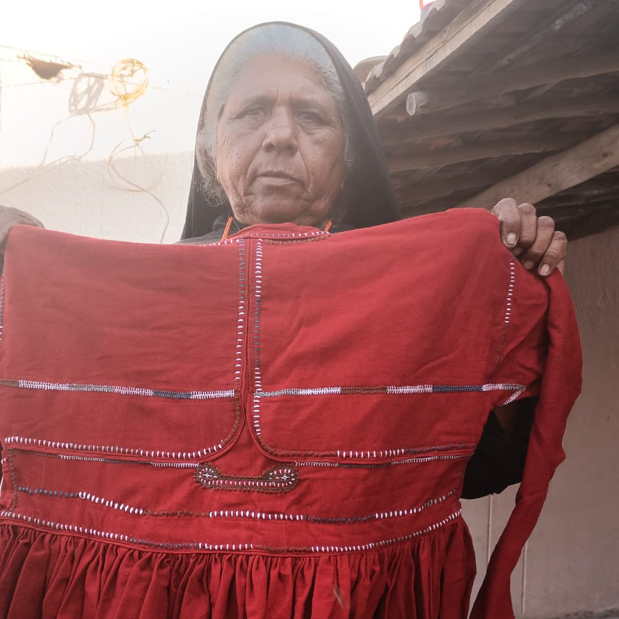 Person holding a red embroidered dress outdoors.