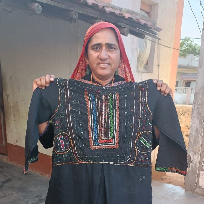 Person holding a black embroidered dress in front of a building